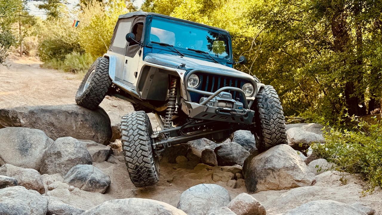 A rock crawler Jeep flexing its suspension over large boulders
